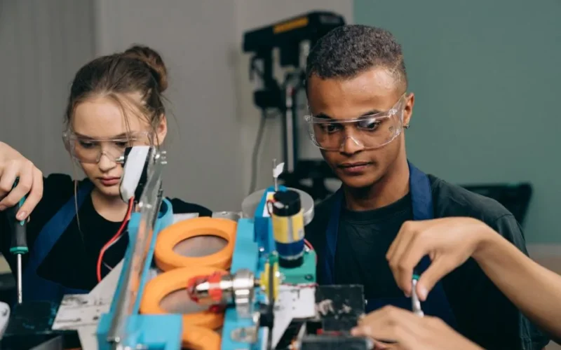 Two young engineers focusing on a robotics project indoors, showcasing teamwork and technology.