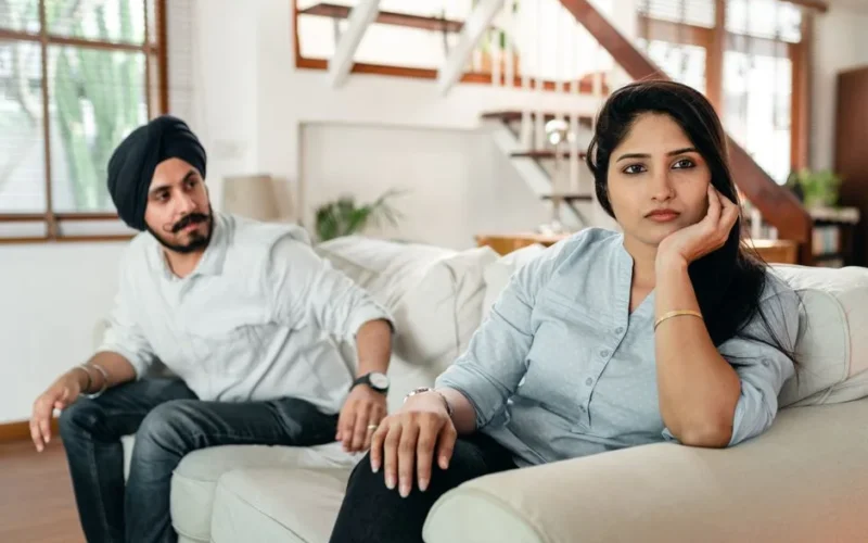 A thoughtful couple engaged in a deep discussion on a vibrant orange sofa in a modern living room.