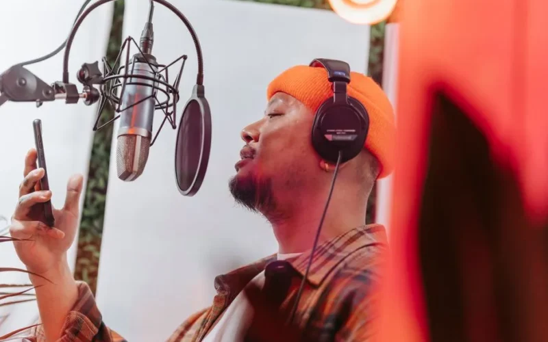 A young musician passionately singing in a recording studio with headphones and microphone setup.
