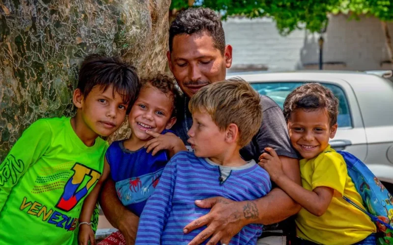 A joyful family moment as a father hugs his smiling children outdoors.