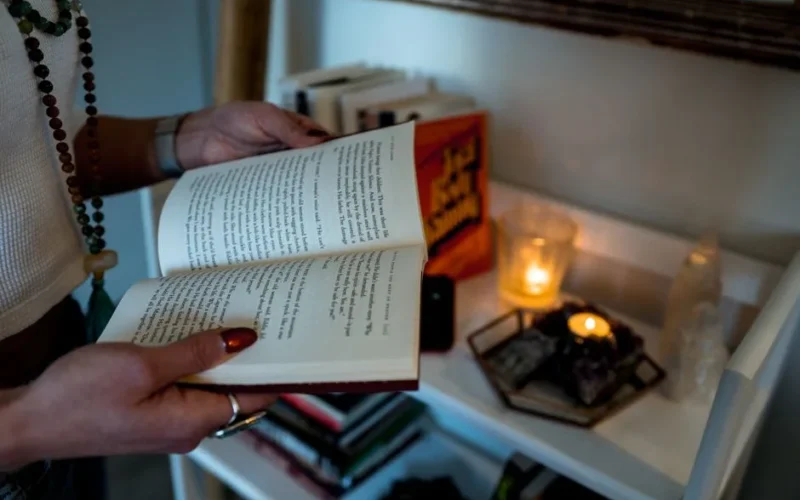 A woman reads an open book by candlelight in a cozy indoor setting. Warm and serene atmosphere.