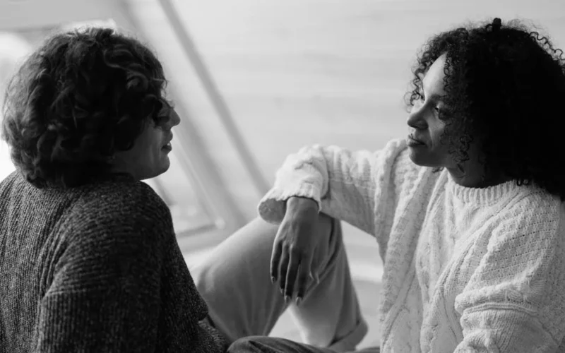 A couple in knitted sweaters sits face to face, engaging in a heartfelt conversation indoors.