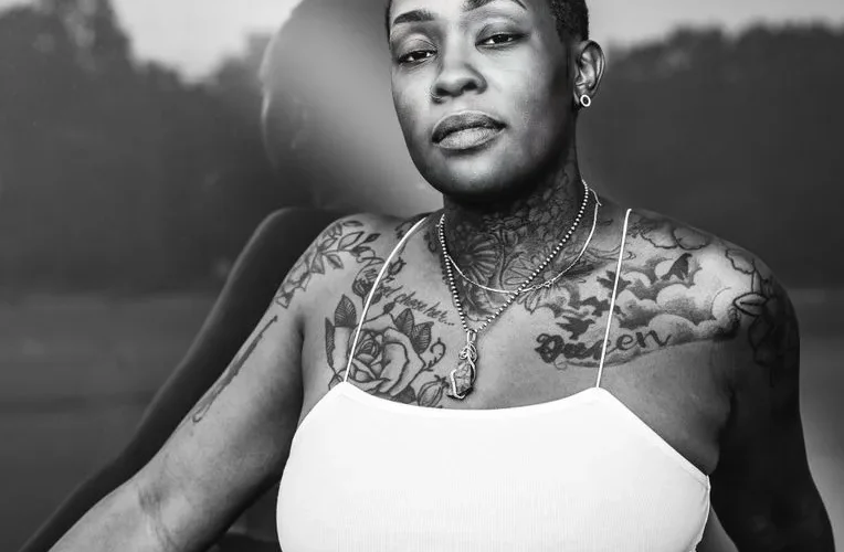Grayscale portrait of a tattooed woman in a white tank top, exuding confidence.
