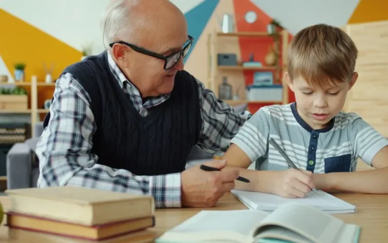 Senior man assisting young boy with schoolwork indoors, fostering learning.