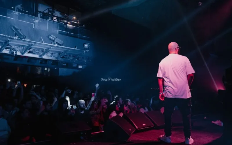 Rapper performing live on stage with vibrant lighting and engaged audience in a concert setting.