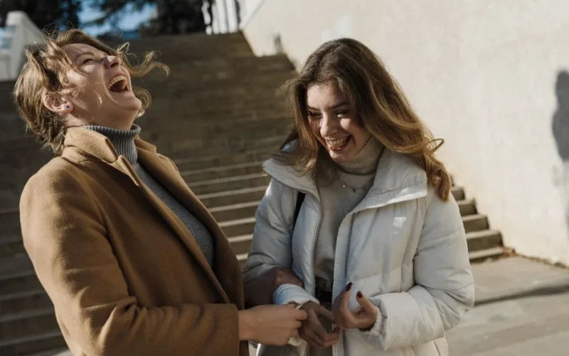 Two young women laughing together outside on a sunny day.
