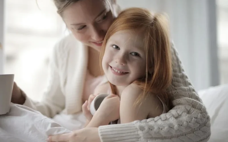 Warm indoor portrait of a mother embracing her young daughter, sharing a cozy moment.