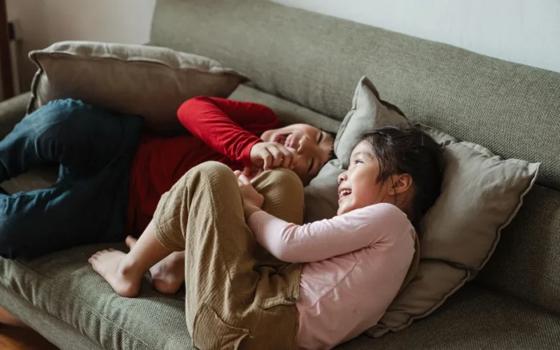 Two children joyfully laughing on a sofa, showcasing happiness and sibling bond.