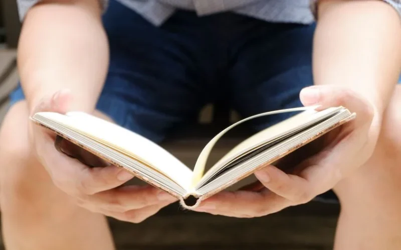 A man casually reads a book while sitting outdoors, showcasing a relaxed lifestyle.