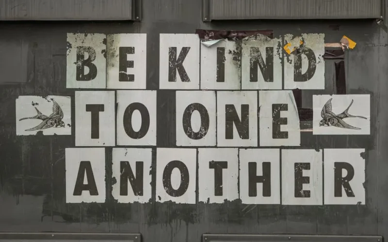 Close-up of 'Be Kind to One Another' message on a weathered background.