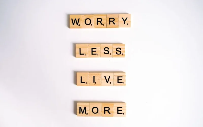 Flat lay of motivational phrase 'worry less live more' on white background using Scrabble tiles.