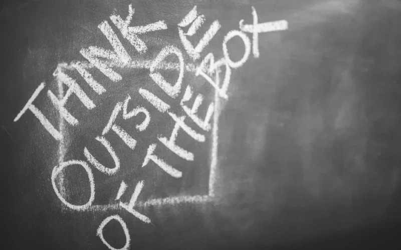 Chalkboard with 'Think Outside the Box' handwritten, inspiring creativity.