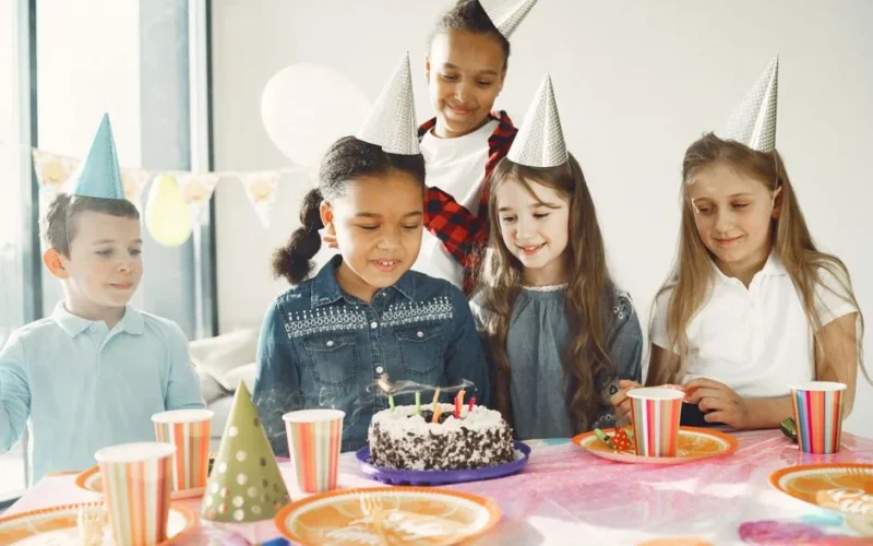 A group of diverse kids celebrating a birthday with cake and party hats.