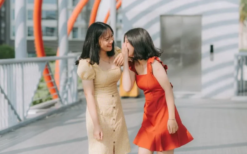 Two young women laughing and sharing a secret outdoors, exuding happiness and friendship.