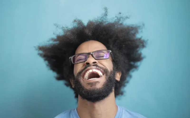 Close-up of a happy man with glasses and wild hair laughing against a blue background.