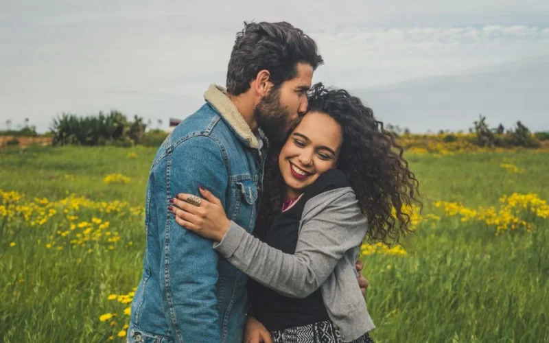 Happy young couple hugging in a sunny field surrounded by flowers, conveying love and joy.