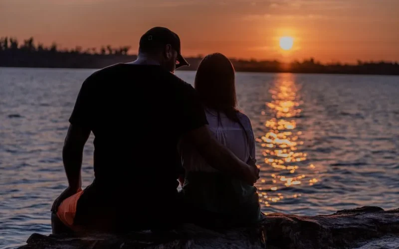 A couple shares a romantic embrace by the seaside during a stunning sunset, reflecting love and tranquility.