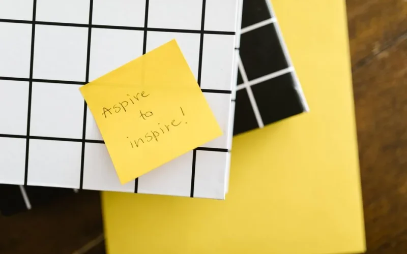 Motivational quote 'Aspire to inspire' on a sticky note placed on books. Minimal and inspirational visual.