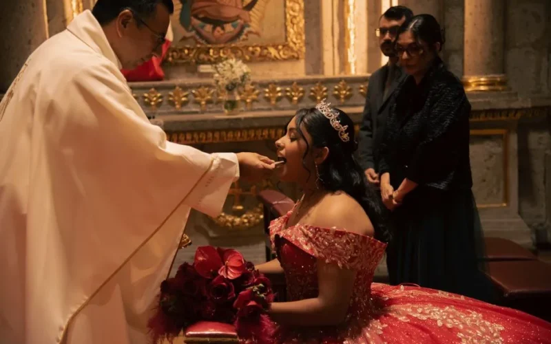 Young woman in red gown receives communion during her quinceañera in a beautifully decorated church.