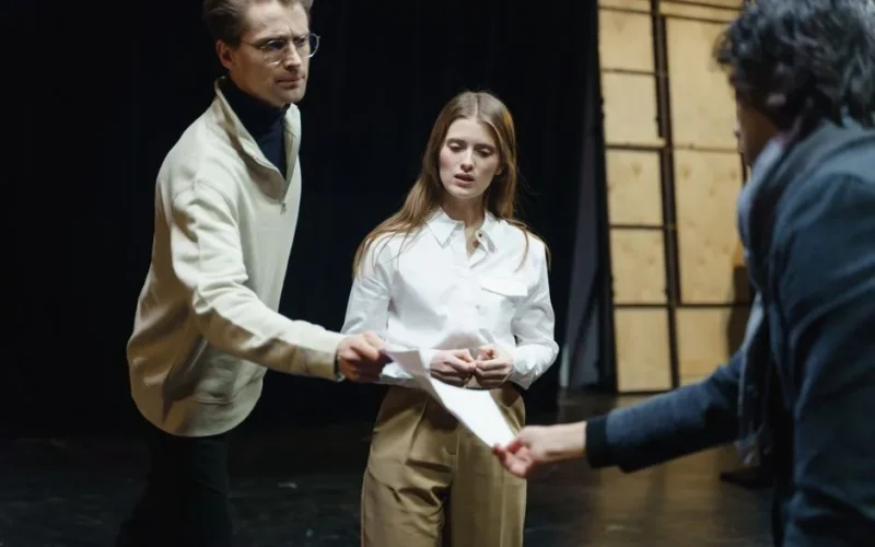 Actors engage in a rehearsal, exchanging scripts on stage, embodying theatrical drama and emotion.