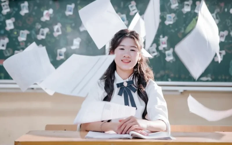 Happy student throws papers in classroom in celebration of school year ending. Cheerful academic success.
