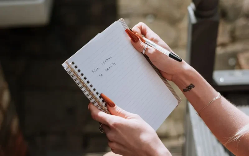 Crop anonymous female with notebook with handwriting saying inspirational words on blurred background in daytime