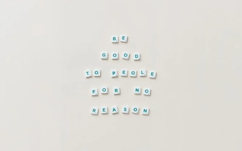 Scrabble tiles spell 'Be good to people for no reason' on a white background.