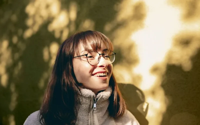 Portrait of a young woman with glasses enjoying sunlight outdoors, capturing a joyful moment.