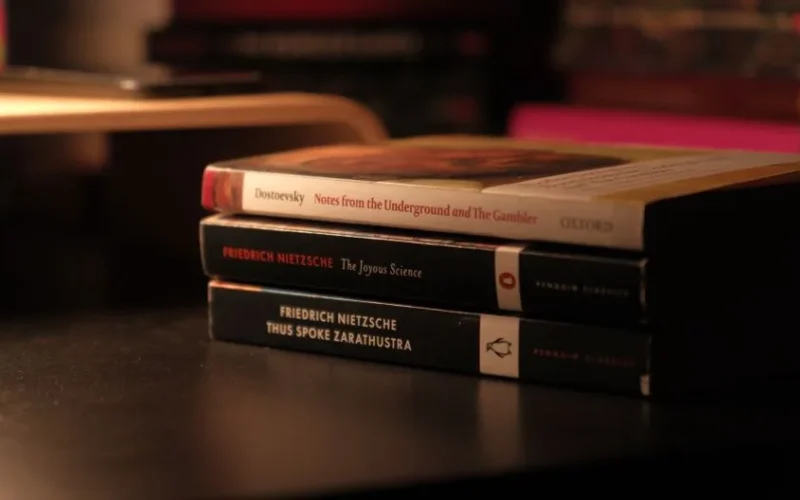 Stack of classic books by Dostoevsky and Nietzsche on a dark desk.