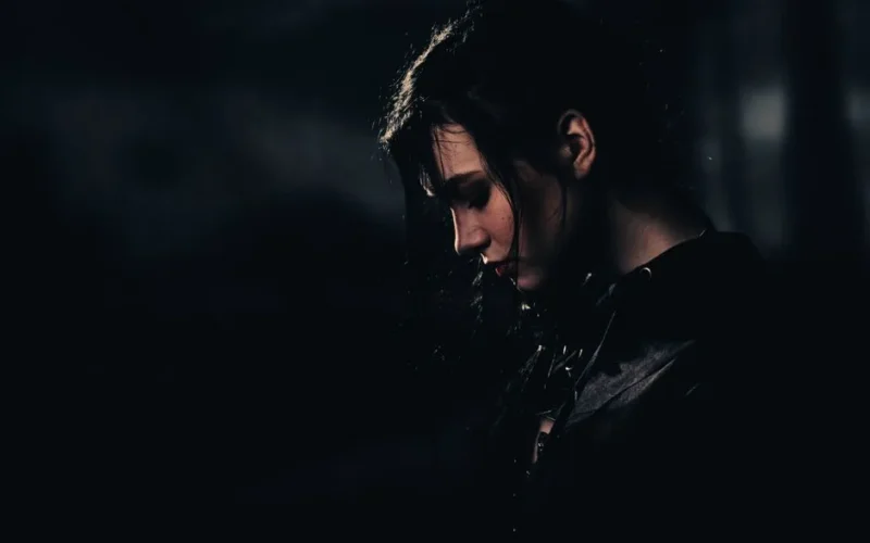 A dramatic portrait of a woman with black hair in a dark setting, evoking mystery and contemplation.
