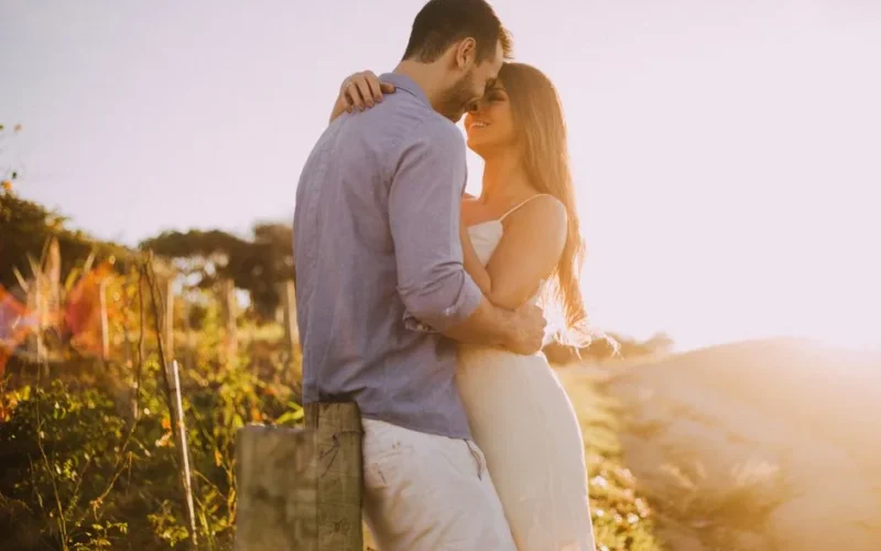 A couple shares a romantic moment embracing at sunset outdoors with warm light.