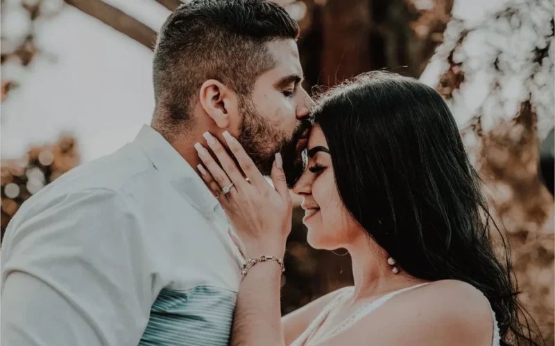 Tender moment of a couple sharing a forehead kiss outdoors, capturing love and serenity.