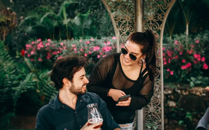 Two young adults laughing and enjoying drinks in a lush garden setting.