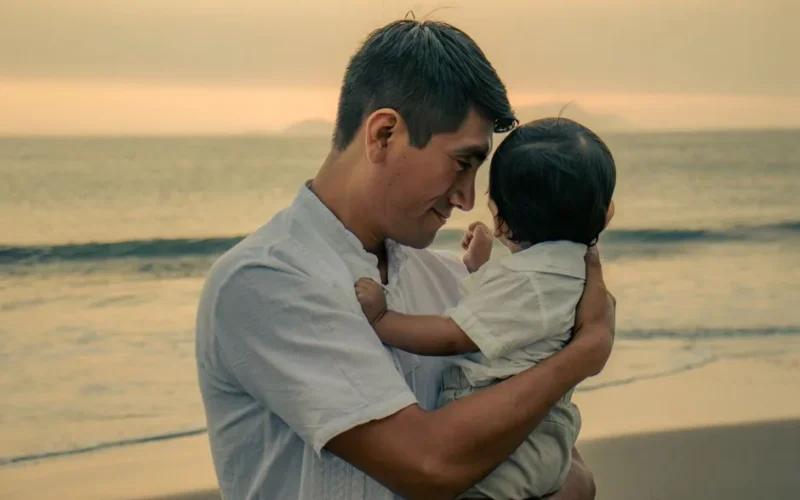Heartwarming moment of a father holding his child by the ocean at sunset, showcasing love and connection.