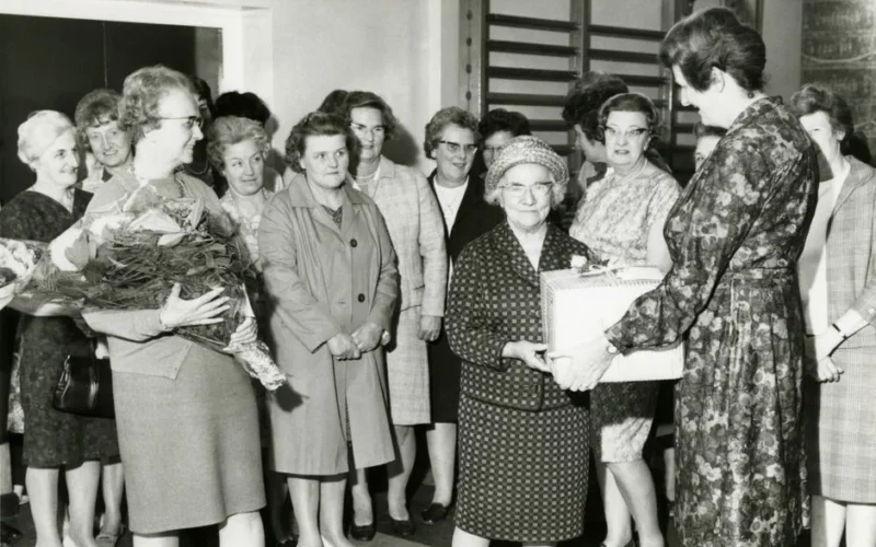 A group of elderly women in a vintage award ceremony receiving gifts and flowers.