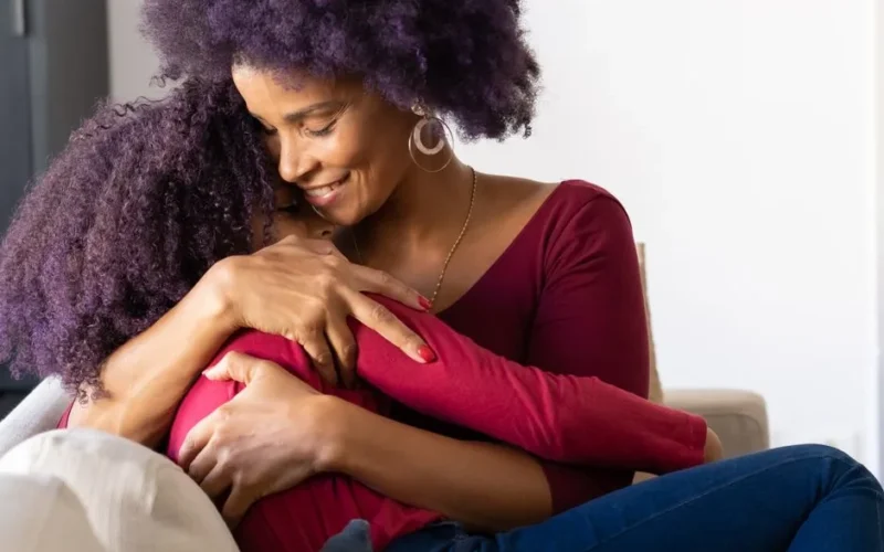A joyful mother embraces her daughter on a cozy sofa indoors, creating a warm and loving scene.
