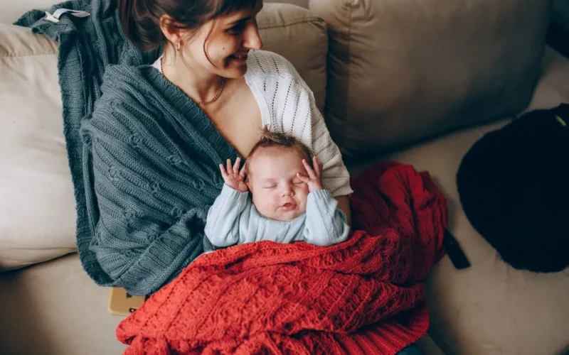 A tender moment of a mother holding her sleeping baby wrapped in a warm blanket indoors.