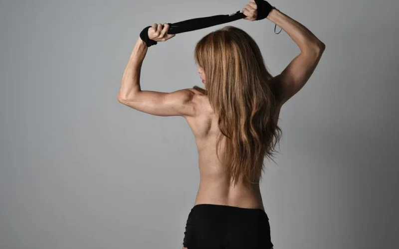 Strong and confident woman showcasing fitness and style in a clean studio environment.