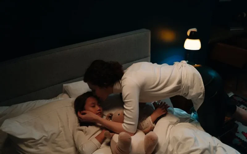 A mother tenderly kisses her sleeping child goodnight in a warmly lit bedroom, creating a peaceful scene.