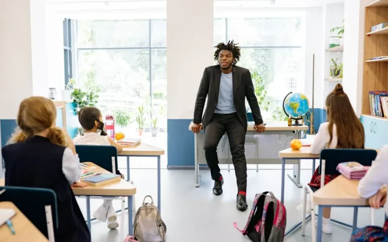 A teacher engages with students in a bright, modern classroom setting, promoting education.