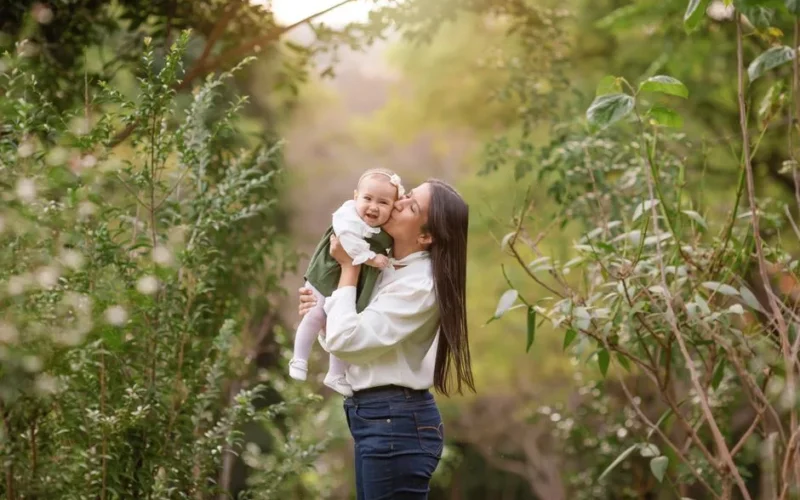 Joyful moment of a mother holding her smiling baby daughter in a lush green outdoor setting.