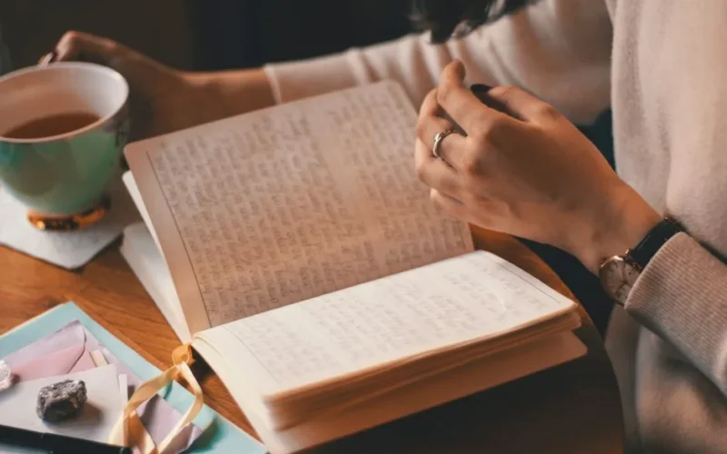 A woman writes in a journal while enjoying a cup of coffee at a wooden table.
