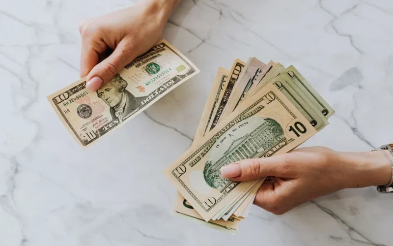 Close-up of hands counting US dollar bills on a marble background, highlighting financial theme.
