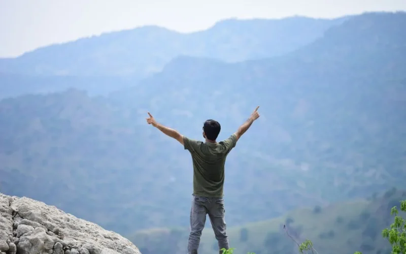 Back view of a man raising arms in victory atop a mountain with stunning views.