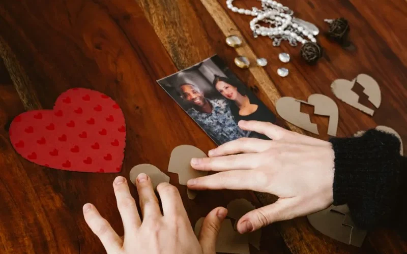 Close-up of hands arranging broken hearts near a couple's photo on a wooden table.