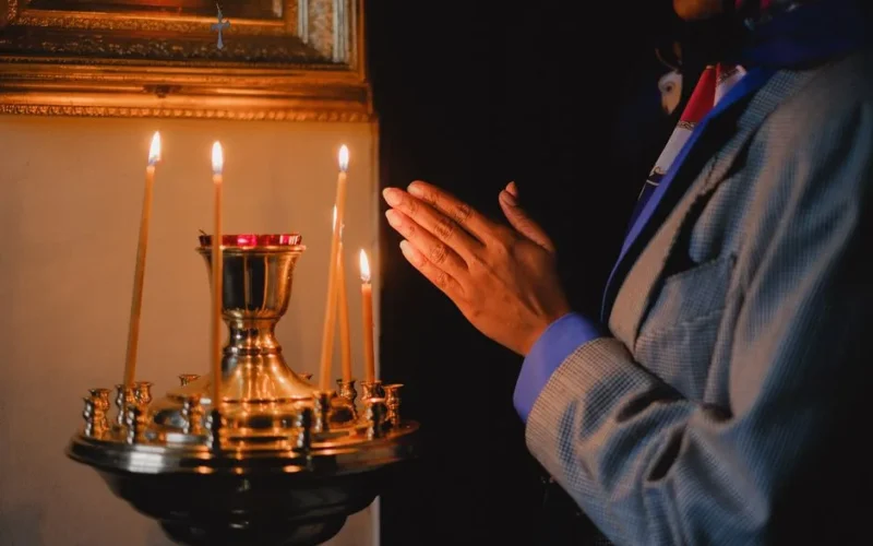 A person praying beside lit candles in a religious setting, evoking peace and spirituality.