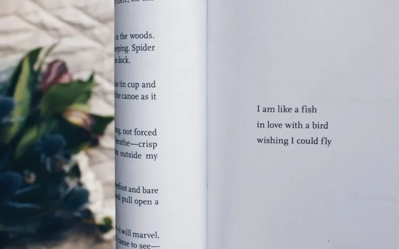 An open book with a poetic quote next to blurred flowers on a rustic surface.