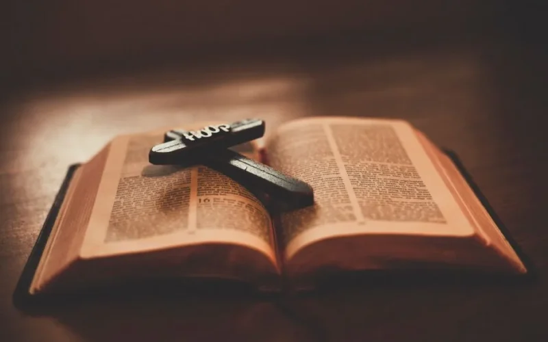 Close-up of an open Bible with a wooden cross inscribed with 'Hope' on a table.