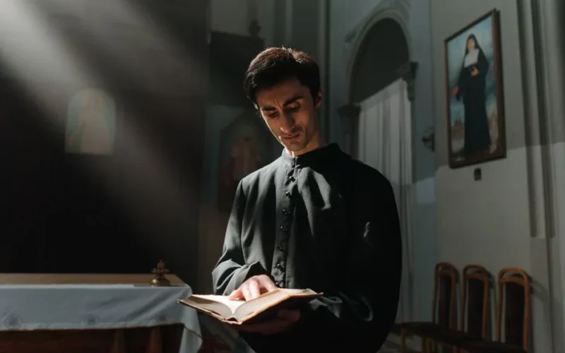 A priest reading a holy book in a church, illuminated by soft light.