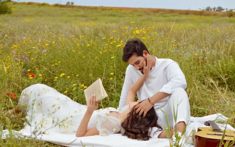 A couple enjoys a romantic moment in a blooming spring field, reading and relaxing.